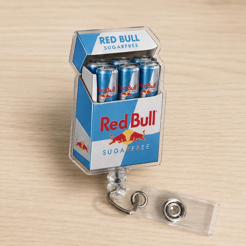 K&ouml;nnte beinhalten: Ein ausziehbarer Ausweishalter mit einem rechteckigen Miniatur-Schachteldesign, das das Red Bull Sugarfree Logo und Branding tr&auml;gt. Die Schachtel enth&auml;lt f&uuml;nf kleine, zylindrische silber-blaue Dosen mit Red Bull Branding und einen transparenten Clip.