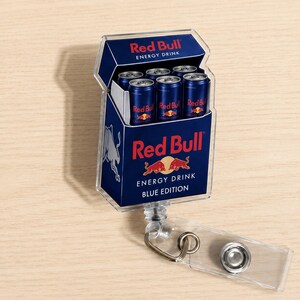 K&ouml;nnte beinhalten: Ein rechteckiger Ausweishalter aus Acryl mit einer Grafik einer Red Bull Energy-Drink-Packung. Das Design zeigt das blau-silberne Branding, das Red Bull-Logo und den Text Red Bull Energy Drink Blue Edition mit sechs Miniaturdosen.