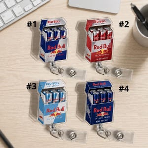 K&ouml;nnte beinhalten: Vier einziehbare Ausweishalter mit Miniatur-Verpackungsdesigns von Red Bull Energy Drinks. Jeder Halter zeigt eine Schachtel mit winzigen Dosen, beschriftet mit #1, #2, #3 und #4, die die Sorten Original, Red Edition, Sugarfree und Blue Edition darstellen.