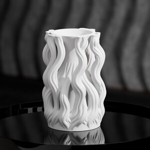 May include: A matte white cylindrical vase featuring a series of vertical, wavy, ribbon-like protrusions that extend from the top rim to the base, creating a textured, organic exterior surface with a hollow centre and a smooth, circular opening.