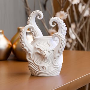May include: A matte white ceramic vase featuring a sculpted octopus design with multiple tentacles curling upward around the rim. The body of the vase displays intricate relief patterns of swirling waves and a central creature face with sharp features.
