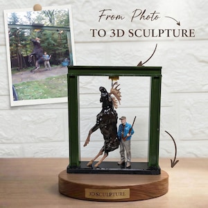 Op de afbeelding: Een 3D-sculptuur met een donkerbruine eland en een figuur in een blauw jasje en beige broek onder een groen metalen frame. Het beeld staat op een ronde houten voet met een gouden plaatje met de tekst 3D SCULPTURE.