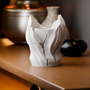 May include: A matte white cylindrical vessel featuring a jagged, vertical split down the center. The exterior surface is composed of layered, organic, leaf-like protrusions that wrap around the central core, creating a textured, sculptural appearance.