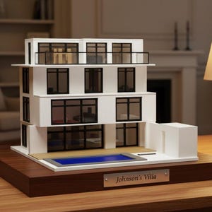May include: A white architectural model of a three-storey villa with black window frames, a balcony, and a rectangular blue swimming pool on the ground level. A silver plaque on the wooden base displays the text Johnson's Villa in black lettering.