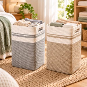 Puede incluir: Dos cestas de lavandería rectangulares hechas de cuerda enrollada. Una cesta es gris y blanca con asas laterales integradas, llena de textiles doblados. La segunda cesta es beige y blanca con asas laterales integradas, llena de textiles.