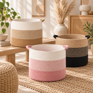 Peut inclure: Trois paniers de rangement cylindriques en corde tressée. Un panier présente des bandes horizontales blanches, beige et marron avec des anses beige. Un autre a des bandes blanches et roses avec des anses roses. Le troisième a des bandes beige et noires.