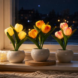 May include: Three tulip flower arrangements in white ceramic pots sit on a windowsill. The tulips have yellow, orange, and pink petals with green leaves. The background shows a nighttime view with city lights.