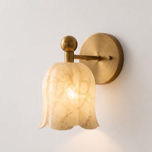May include: A wall sconce featuring a bell-shaped, translucent, cream-colored glass shade with a marbled texture. The fixture includes a circular brass-toned mounting plate and a short, straight arm connecting to the glass shade via a small sphere.