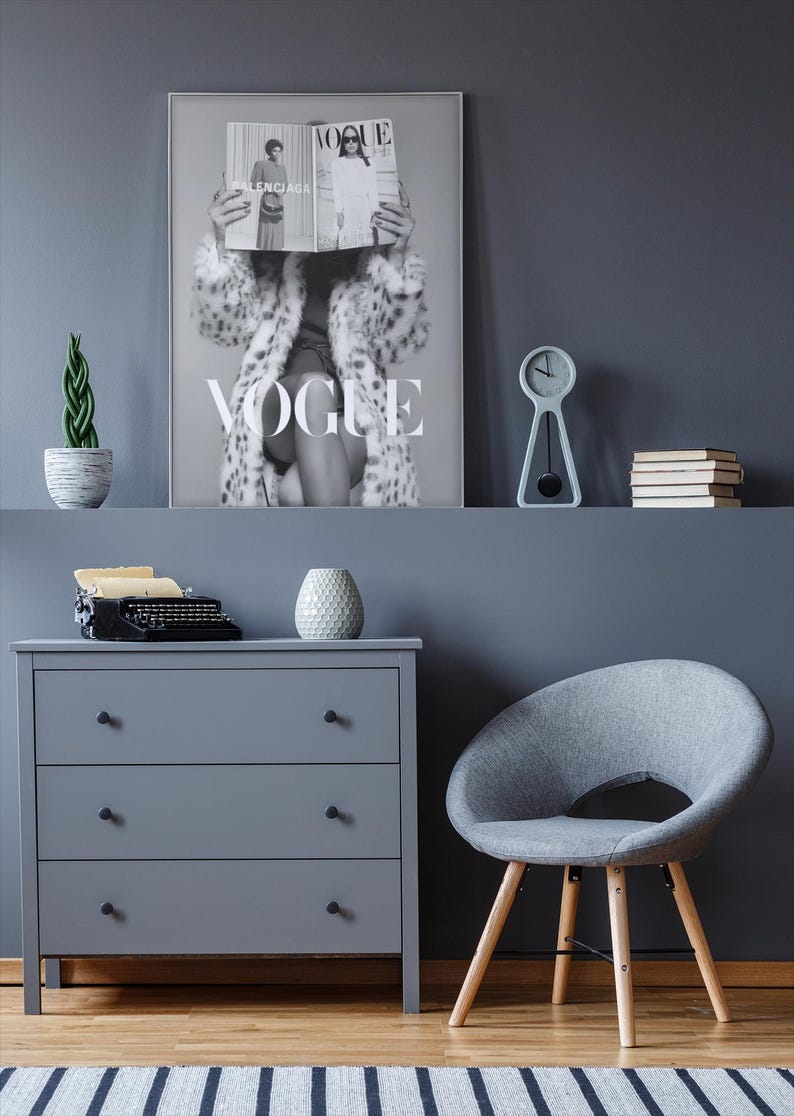 May include: A framed black and white wall art print featuring a person holding a Vogue magazine in front of their face, wearing a patterned coat. The print displays the word VOGUE in large white letters and is displayed on a dark gray wall.