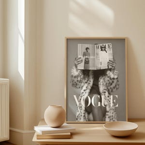 May include: A framed black and white wall art print featuring a person wearing a leopard print coat and holding a Vogue magazine in front of their face. The magazine cover displays the text Vogue and Balenciaga in a clear, bold typeface.