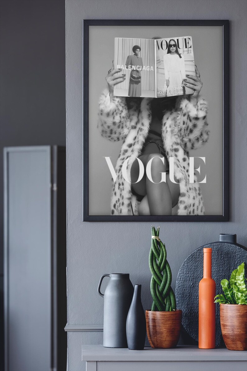 May include: A black and white framed wall art print featuring a person wearing a leopard print coat, holding a Vogue magazine open in front of their face. The magazine displays the text Balenciaga and Vogue. The word VOGUE is printed in large white letters across the center of the artwork.