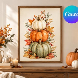 Op de afbeelding: Een ingelijste muurkunstprint met een verticale stapel van drie pompoenen in wit, oranje en saliegroen, omringd door herfstbladeren en rode bessen. De illustratie staat op een crèmekleurige achtergrond in een houten lijst.