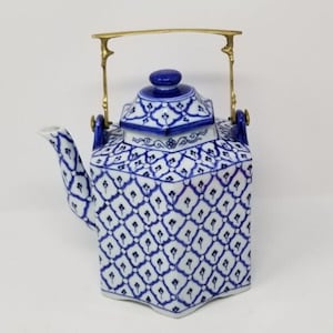 May include: A blue and white ceramic teapot with a geometric pattern. The teapot has a gold-colored handle and a blue knob on the lid. The spout and handle are blue. The teapot is likely used for serving tea.