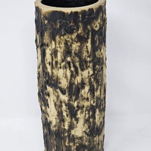May include: A tall, cylindrical vase with a textured surface, resembling tree bark. The vase features a dark brown, almost black, exterior over a lighter tan base. The interior is a dark, glossy color. A decorative home accent.