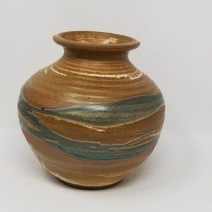 May include: A handcrafted ceramic vase with a rounded body and a narrow neck. The vase features a warm brown base color with horizontal bands of brown, teal, and white. The vase is approximately 7 inches tall.