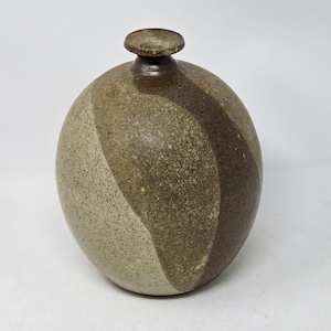 May include: A spherical ceramic vase with a narrow neck and a flat, circular rim. The surface features a speckled, textured finish in shades of beige, tan, and dark brown, with a distinct diagonal band of darker brown color across the body.