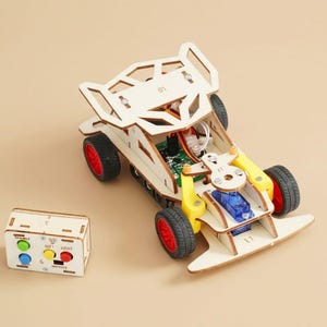 May include: A DIY remote-controlled car kit made of light-colored wood with four black wheels featuring red rims. The vehicle includes a green circuit board, a blue servo motor, and yellow plastic components. A matching wooden remote control has four buttons.
