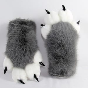 May include: A pair of plush animal paw gloves featuring long grey faux fur on the back and white faux fur on the palm side. Each glove has four rounded white padded toes and sharp, curved black plastic claws attached to the tips of each digit.