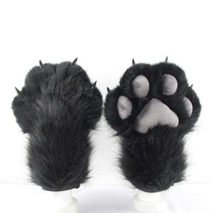 May include: A pair of black faux fur gloves designed as animal paws. One glove shows the long black fur with sharp black claws, while the other displays the palm side featuring soft grey padded paw pads and matching black claws.