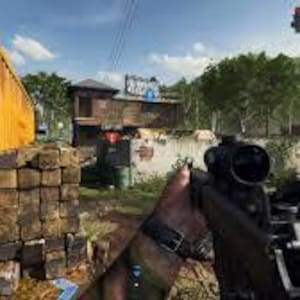 May include: First-person view of a rifle with a scope, held by a person in a camouflage sleeve. The scene is set outdoors, with a yellow container and a building in the background. The sky is blue with some clouds.