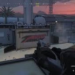 May include: A first-person view of a video game scene with a gun in the foreground. The scene features a building with the word "Z" in red on the side, set against a dusky sky. Other structures and a palm tree are also visible.
