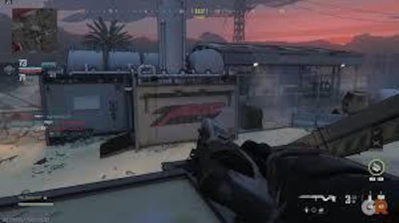 May include: A first-person view of a video game scene with a gun in the foreground. The scene features a building with the word "Z" in red on the side, set against a dusky sky. Other structures and a palm tree are also visible.