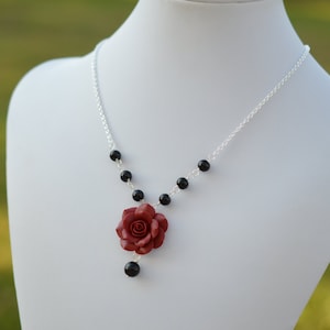 May include: A silver chain necklace with black beads and a red rose charm.
