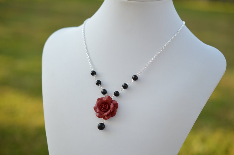 May include: A silver chain necklace with black beads and a red rose charm.