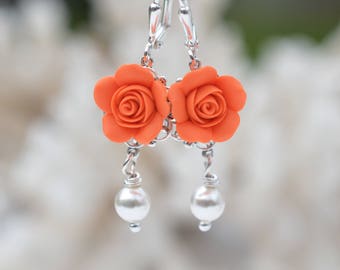 May include: A pair of silver dangle earrings with orange rose-shaped charms and white pearl accents.