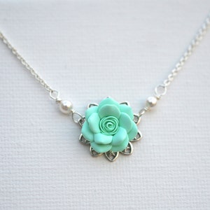 May include: A silver chain necklace with a mint green flower pendant. The flower has a delicate, intricate design and is accented with two small white pearls.