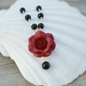 May include: A red rose flower pendant necklace with black beads and a silver chain.