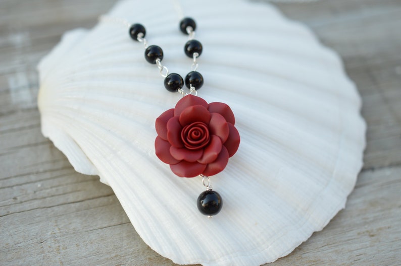 May include: A red rose flower pendant necklace with black beads and a silver chain.