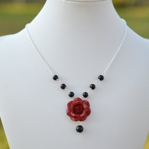 May include: A silver chain necklace with black beads and a red rose charm.