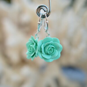 May include: A pair of silver dangle earrings with two light blue polymer clay roses.