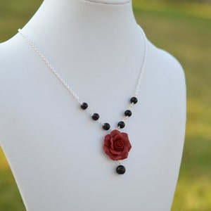 May include: A silver chain necklace with black beads and a red rose pendant.