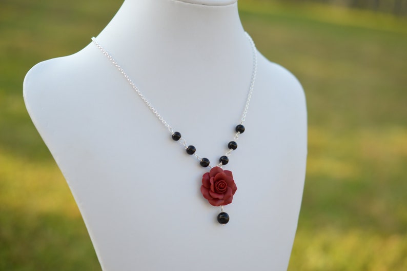 May include: A silver chain necklace with black beads and a red rose pendant.