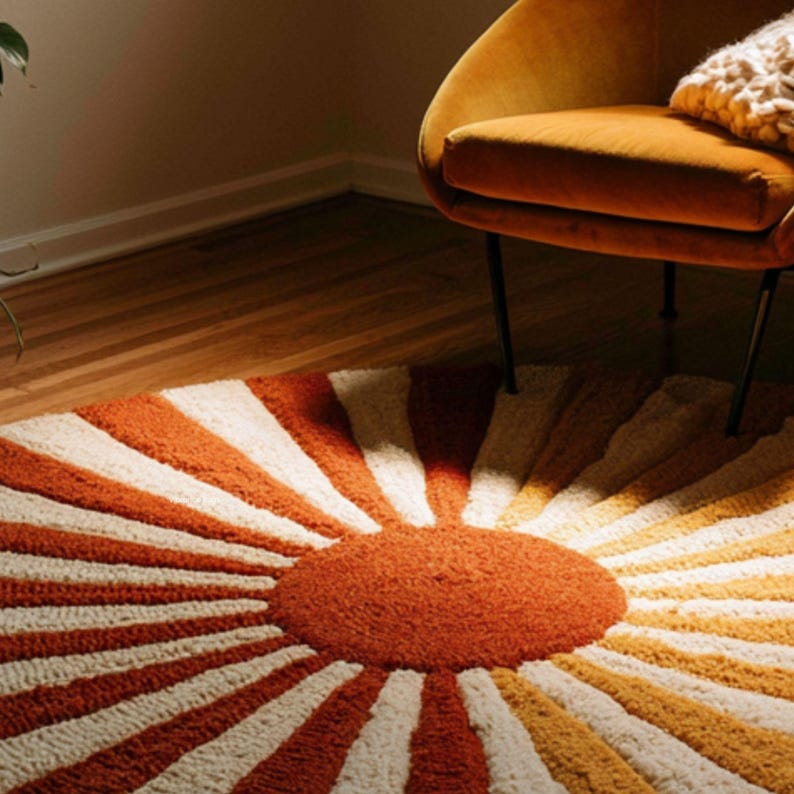 May include: A round, tufted area rug featuring a central orange circle with radiating sunburst stripes in alternating shades of burnt orange, cream, and mustard yellow. The rug has a thick, textured pile and a circular shape that covers the floor.