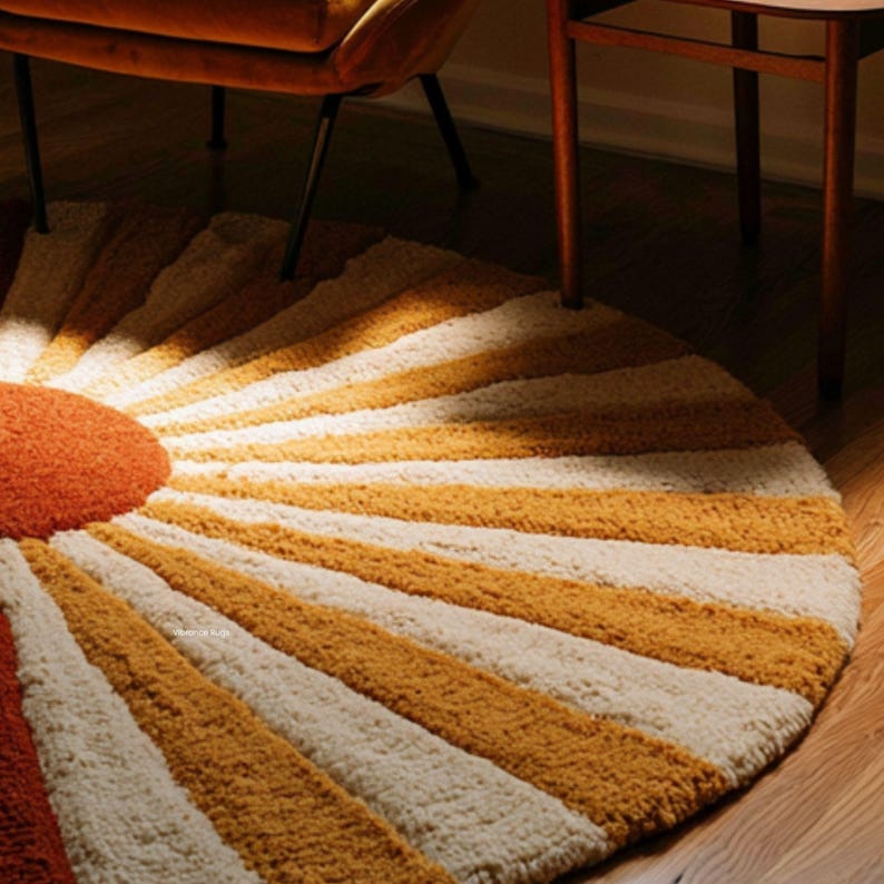 May include: A circular tufted rug featuring a sunburst pattern with a solid burnt orange center and alternating rays of mustard yellow and cream white. The rug has a thick, textured pile surface and is positioned on a wooden floor.