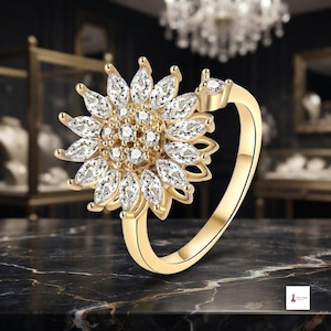 May include: A gold-toned ring featuring a large, sunflower-shaped centerpiece composed of marquise-cut and round-cut clear stones. The band is smooth and polished, with a single small round stone set on the side near the floral arrangement.