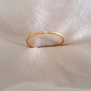 May include: A simple gold band ring with a single small diamond set in the centre.