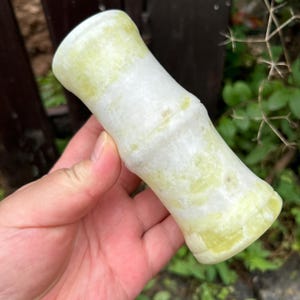 May include: A cylindrical stone object with a smooth, polished surface featuring a marbled pattern of pale yellow and white. The object has a slightly flared top and bottom with a central indentation, resembling the segmented appearance of bamboo.