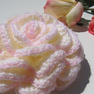 May include: A crocheted flower in shades of pink and white. The flower is made of yarn and has a delicate, layered design.