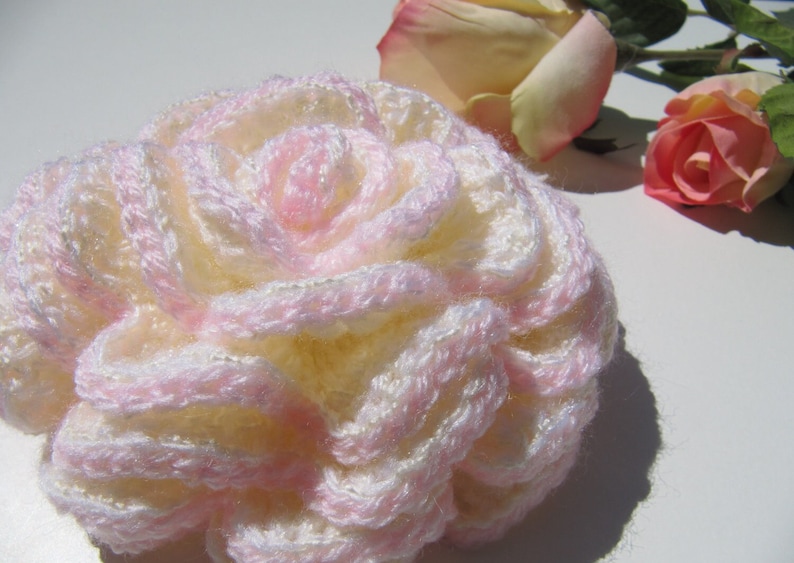 May include: A crocheted flower in shades of pink and white. The flower is made of yarn and has a delicate, layered design.