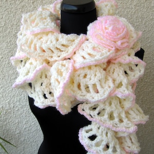 May include: A white crocheted scarf with pink trim and a pink crocheted flower. The scarf is draped over a black mannequin.