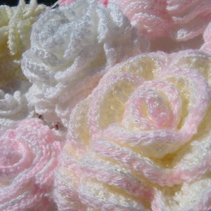 May include: A close-up of a bouquet of crocheted flowers in shades of white, pink, and cream. The flowers are made with a delicate, lacy stitch and have a soft, fluffy texture.