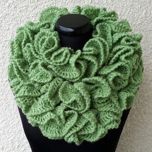 Puede incluir: Una bufanda infinita de ganchillo verde con un diseño de volantes. La bufanda está hecha con un hilo suave y tiene un aspecto delicado y femenino.
