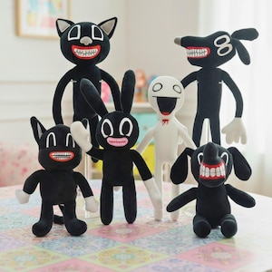 Peut inclure: Ensemble de poupées en peluche représentant des personnages de dessins animés. Les poupées sont noires avec des détails blancs, de grands sourires et des traits animaliers, comme des oreilles de chat, de lapin et de chien. Elles sont disposées sur une surface à motifs.
