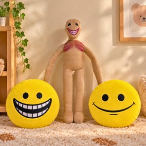 May include: A beige humanoid plush toy with long arms, a wide toothy grin, and reddish chest markings, flanked by two round yellow plush pillows. One pillow features a wide toothy grin, while the other displays a simple black curved smile.