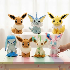 Könnte beinhalten: Eine Sammlung von Pokémon-Plüschfiguren, darunter Evoli, Vaporeon, Blitza, Glaziola, Blättra und Feelinara. Jedes Plüschtier hat einzigartige Merkmale und Farben, mit weichem Fell und detaillierten Designs. Die Figuren werden auf einer pastellfarbenen Oberfläche präsentiert.