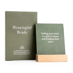 May include: A set of "Meaningful Reads" reflection cards and a matching journal in a muted green color. The journal has the title in white text. The card reads "Telling your story is a gift to those still finding their own."